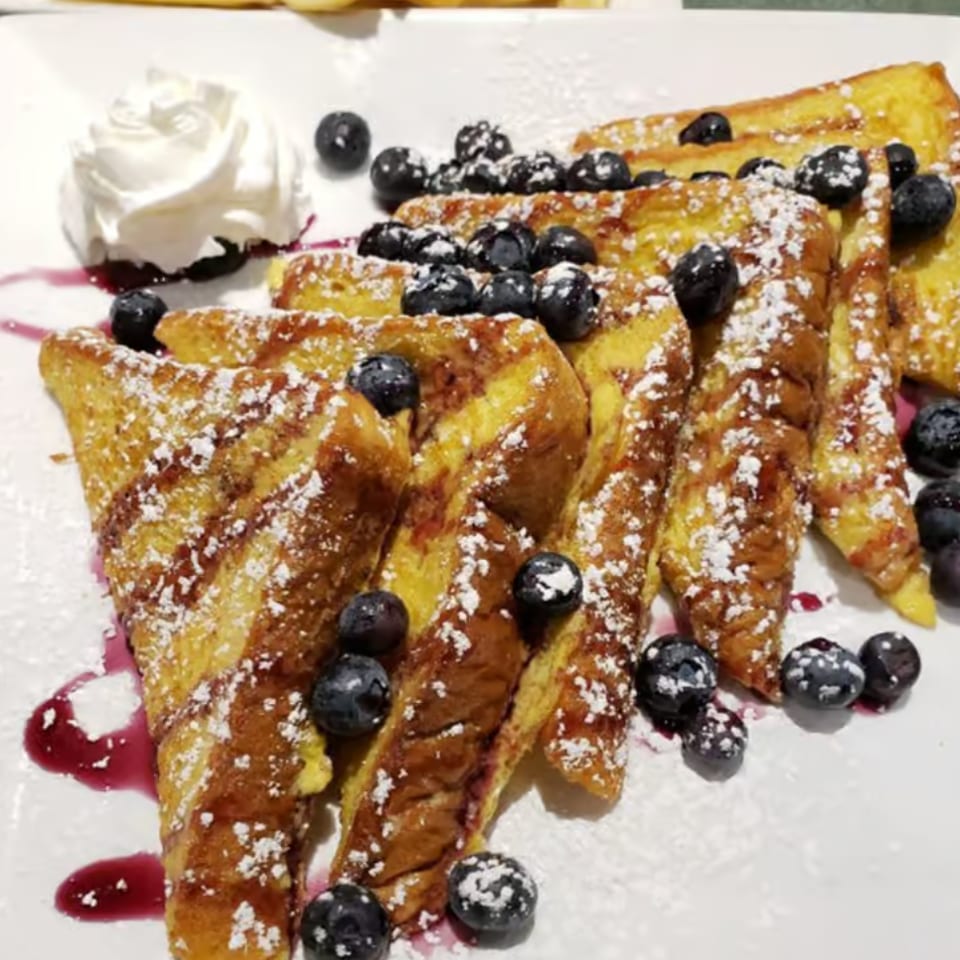 Golden French toast slices topped with blueberries, powdered sugar, and whipped cream on a white plate.