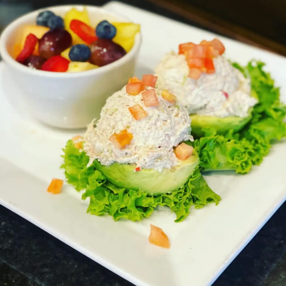 Two avocado halves filled with chicken salad and diced tomatoes, served with a fruit cup.