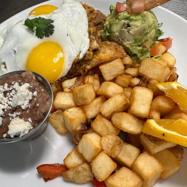 Breakfast plate with fried eggs, home fries, refried beans, guacamole, and a tortilla chip.