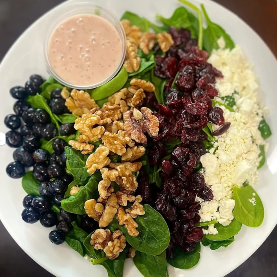 A vibrant spinach salad with blueberries, walnuts, dried cranberries, feta cheese, and dressing.