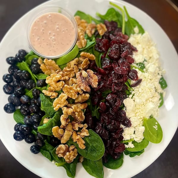 Spinach salad with blueberries, walnuts, dried cranberries, feta cheese, and a side of dressing.