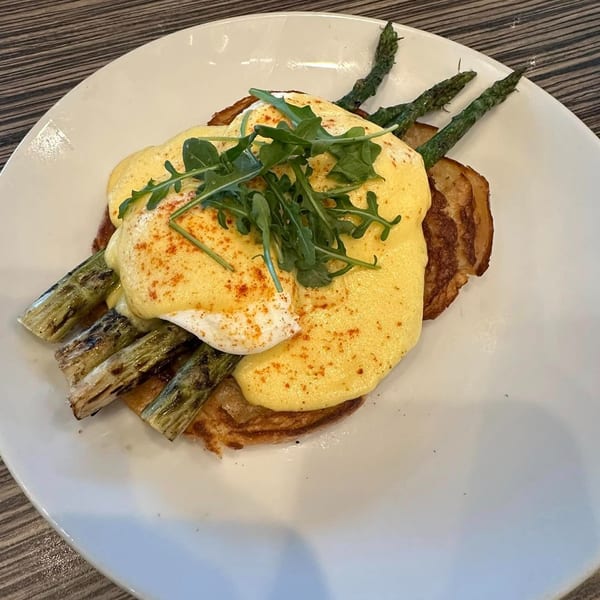 Eggs Benedict with hollandaise sauce, asparagus, and arugula on a white plate.