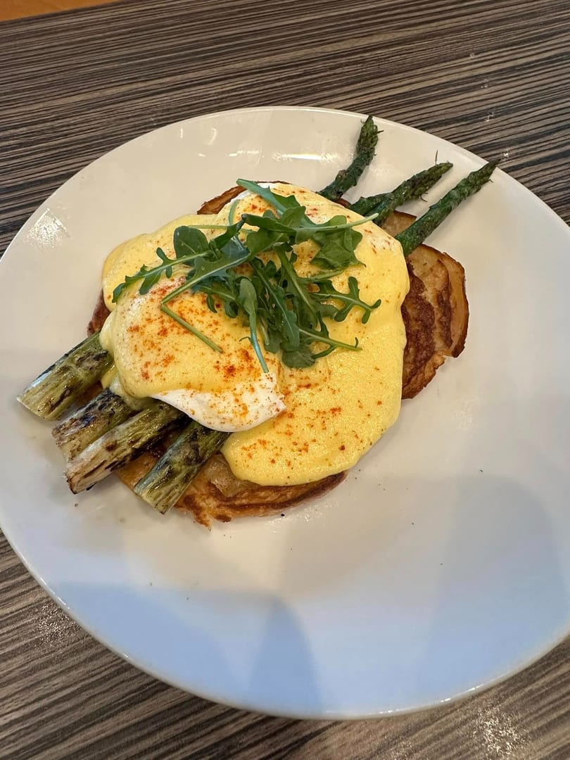 Eggs Benedict with hollandaise sauce, asparagus, and arugula on a white plate.