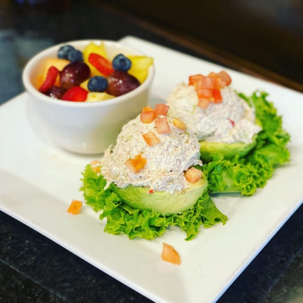 Two avocado halves filled with chicken salad and diced tomatoes, served with a fruit cup.