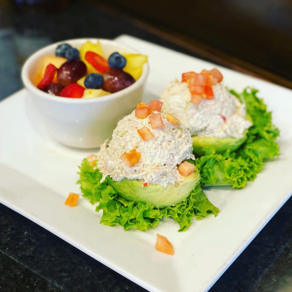 Two avocado halves filled with chicken salad and diced tomatoes, served with a fruit cup.