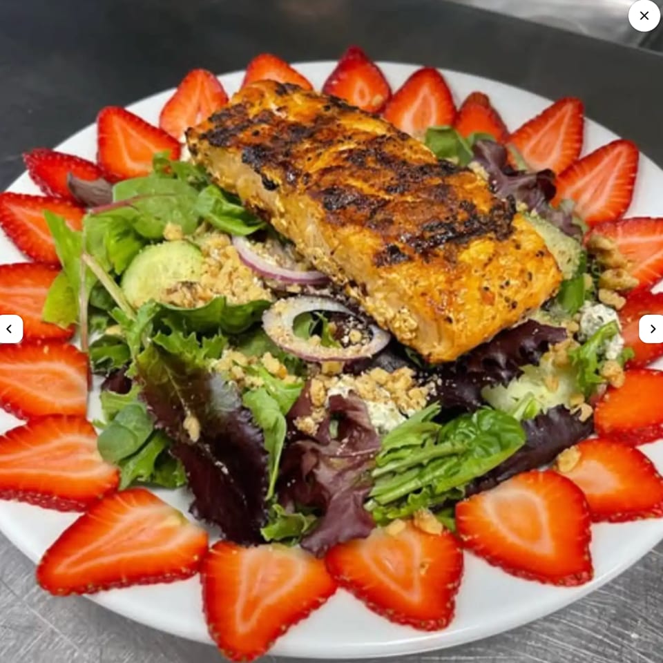 Grilled salmon fillet on a bed of mixed greens, topped with nuts and surrounded by strawberry slices.